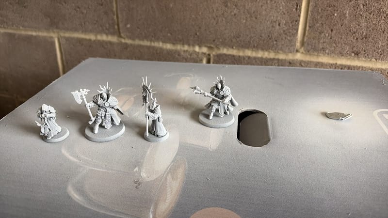 Four Stormcast models freshly sprayed white on top of a cardboard box, outside against a brick wall.