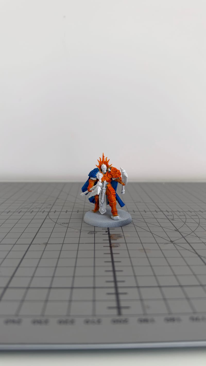 The Reclusian from the front, with orange armour and a blue cloak, standing on a cutting mat.