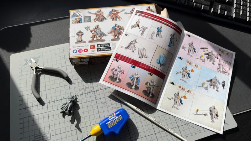 A Reclusian half-built on a cutting mat, next to its open instruction booklet, clippers and a tube of plastic glue.