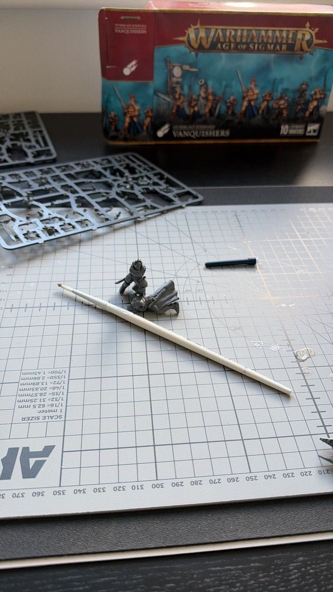 A half-built Vanquisher lying on a cutting mat next to a paintbrush, with two sprues and the Vanquishers box behind.